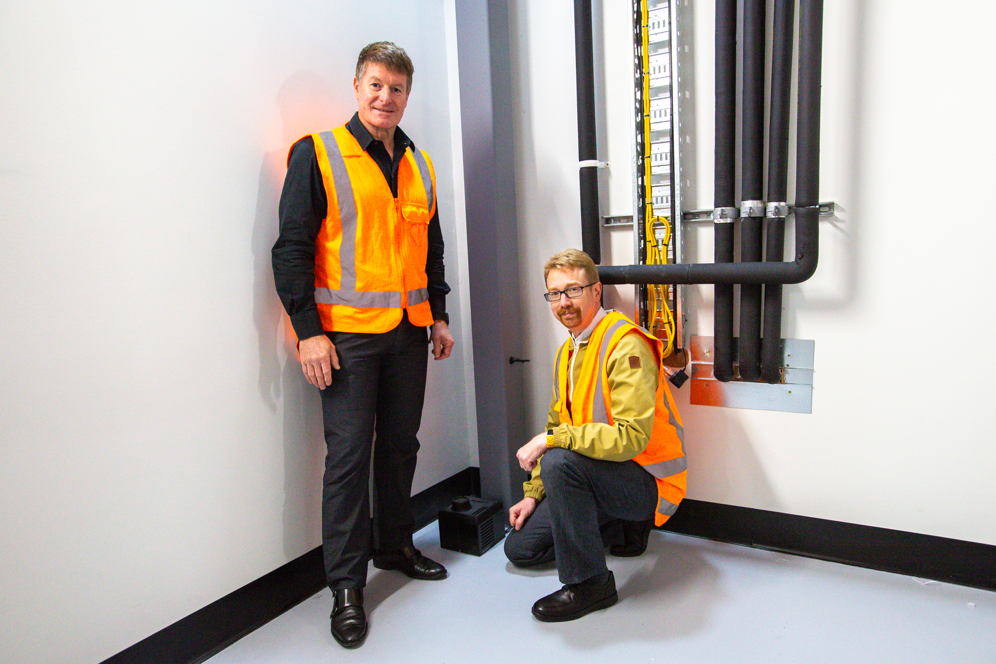 Two engineers in high-visibility vests beside the installed SenseiQ sensor at One New Zealand Stadium.